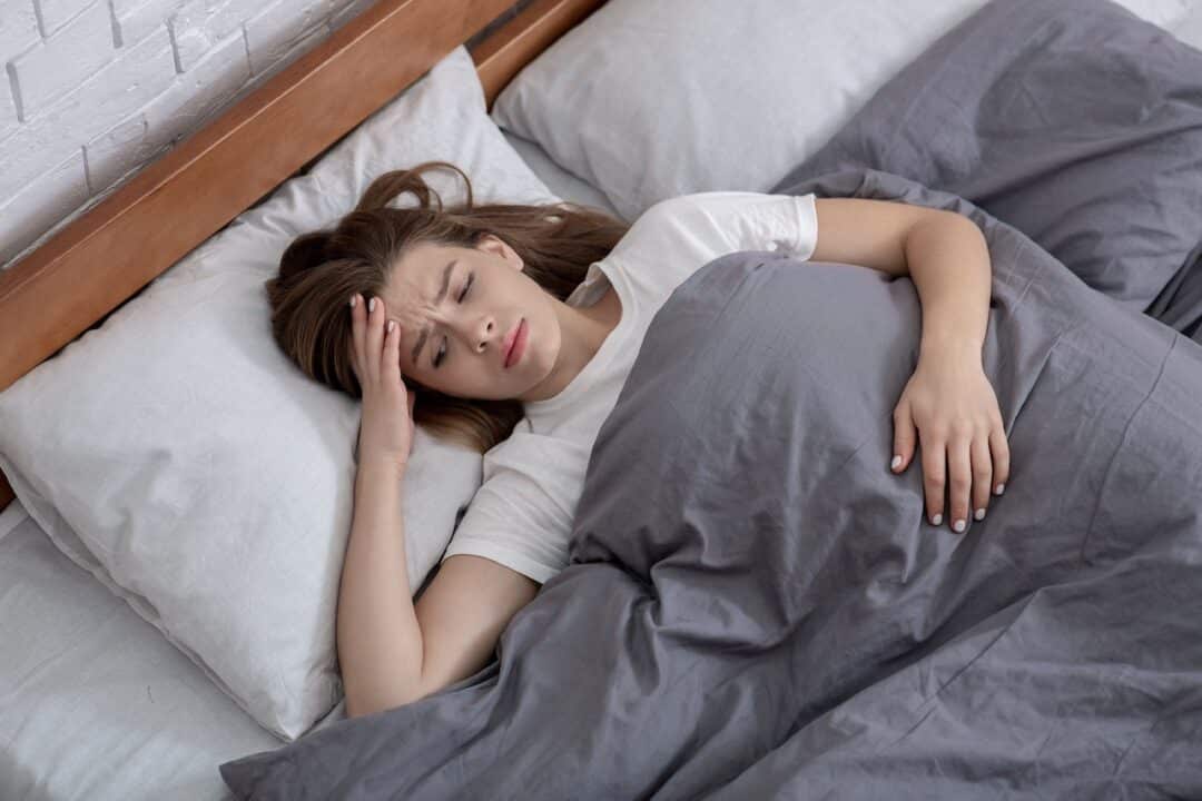 Schlafstörungen machen das Leben schwer. Erfahre mehr zu den Ursachen. Frau liegt mit Schlafstörungen im Bett