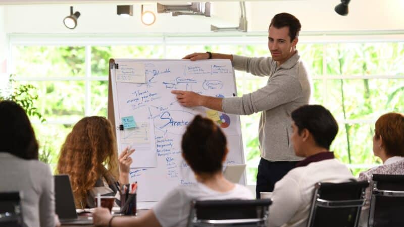 Business man giving presentation on future plans to his colleagues at office Durchsetzungsvermögen im Beruf hilft bei der Karriere.