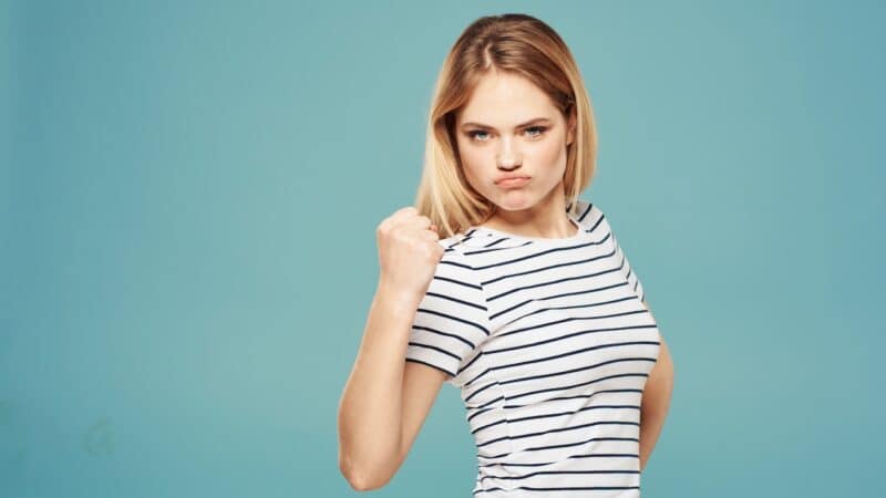 Portrait of a woman on a blue background in a striped T-shirt emotions irritability Durchsetzungsvermögen fühlt sich stark an!